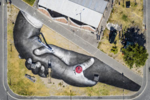 French-Swiss artist Saype poses in one of his giant landart fresco painted for the 9th step of his worldwide "Beyond Walls" project in the Langa township, Cape Town, South Africa, on Friday January 22, 2021. Three frescoes were created using approximately 1000 liters of biodegradable pigments made out of charcoal, chalk, water and milk proteins. The "Beyond Walls" project aims at creating the largest symbolic human chain around the world, promoting values such as togetherness, kindness and openness to the world. Here in Cape Town this step was motivated by the country's persisting need for reunification. Three frescoes representing widely different populations and realities within the city were created in Sea Point (6000 Sq. m), the Philippi township (800 Sq. m) and the Langa township (800 Sq. m). (Valentin Flauraud for Saype - EDITORIAL USE ONLY)