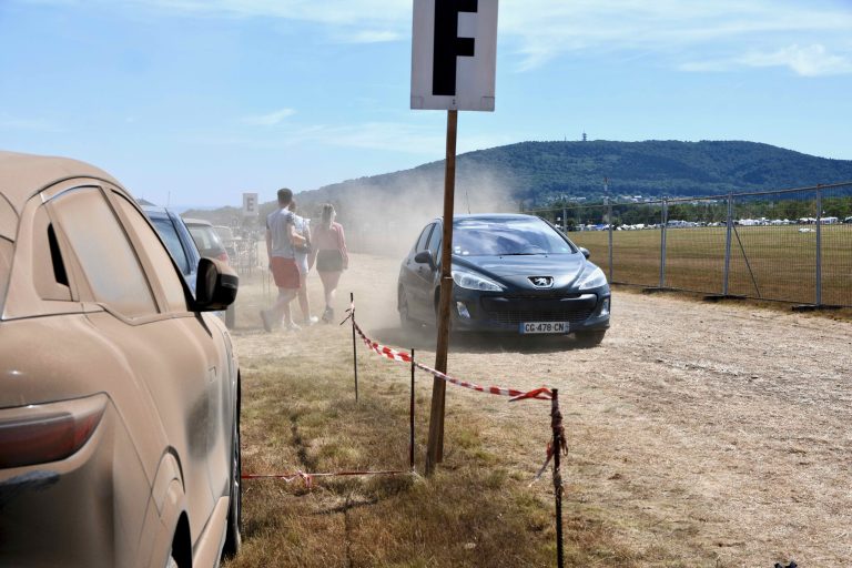 Sur le parking du camping, les voitures des festivaliers sont recouvertes de poussières. | ©Le Trois - A.S.