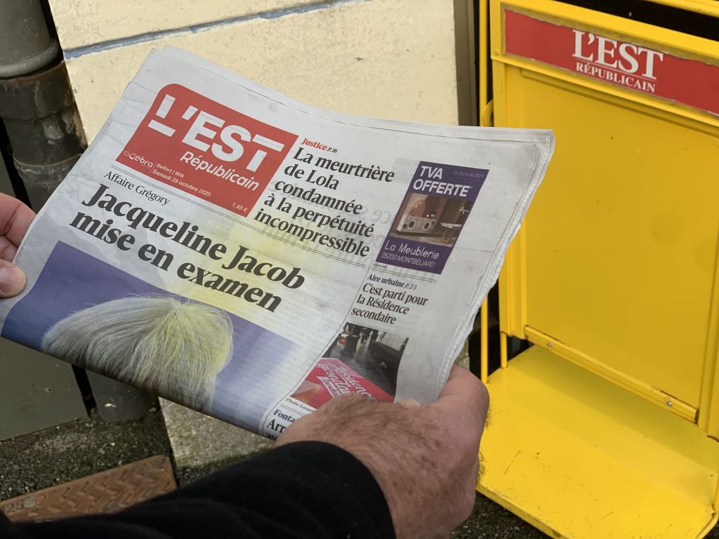 est_républicain Lecture du journal L'Est Républicain, devant un porte affichette.