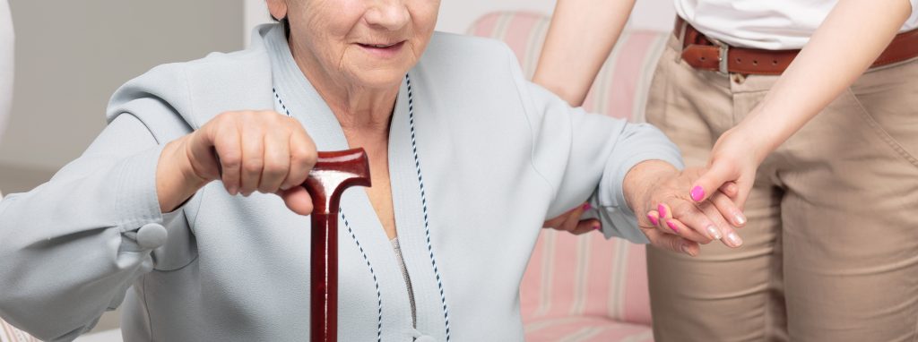 Une jeune femme accompagne une personne âgée pour se lever.