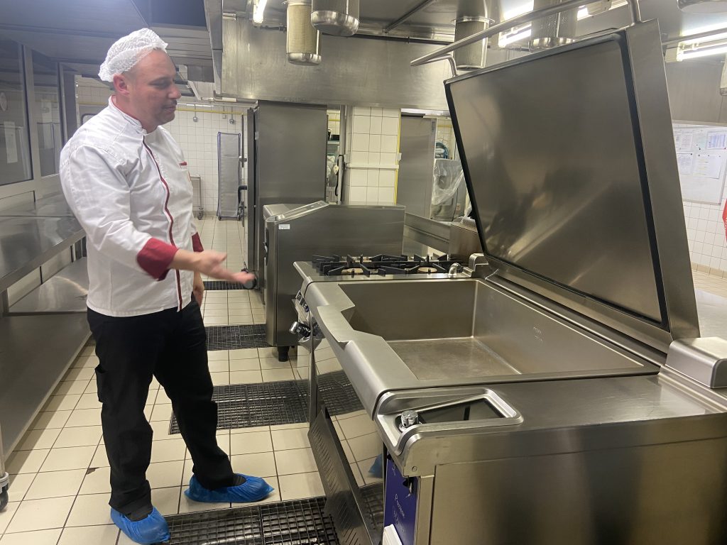 Flavien le Juge devant la sauteuse de la salle de production du Resto U' Duvillard, à Belfort.