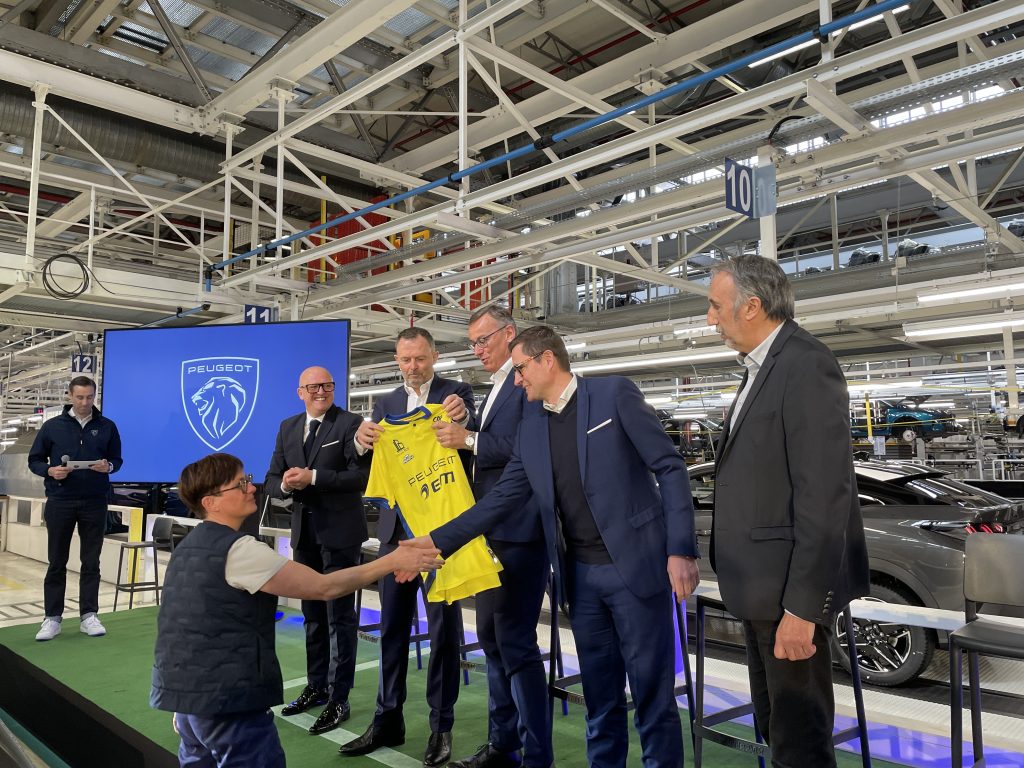 Le nouveau maillot a été apporté par une salariée de l'usine Stellantis de Sochaux, arrivée près de l'estrade en Peugeot 3008 avant de le remettre au président de Peugeot, Alain Favey.