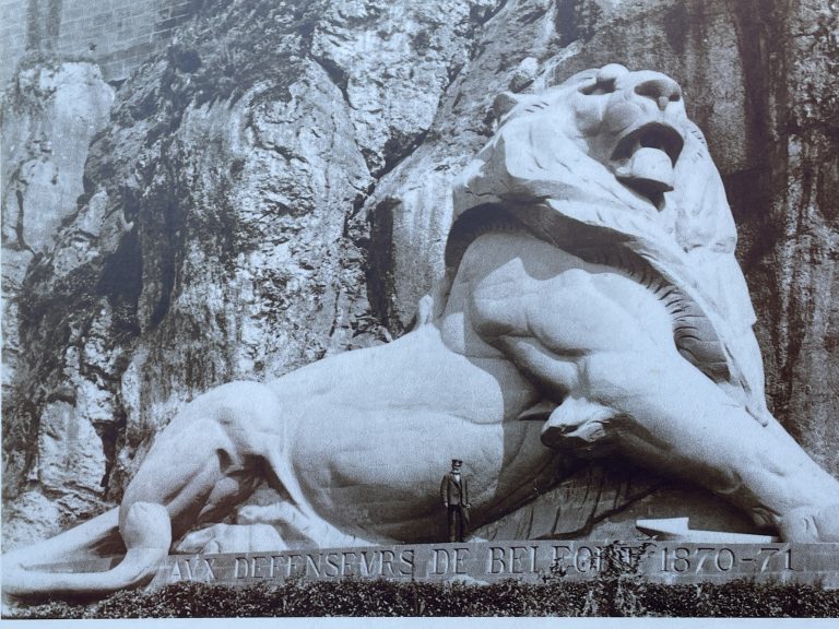 Une reproduction de carte postale du Lion sur un panneau touristique le montre dans son état originel, recouvert de badigeon.