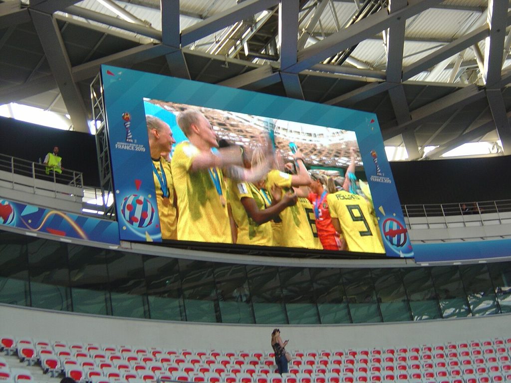 Un écran géant, diffusant du football, dans un stade.