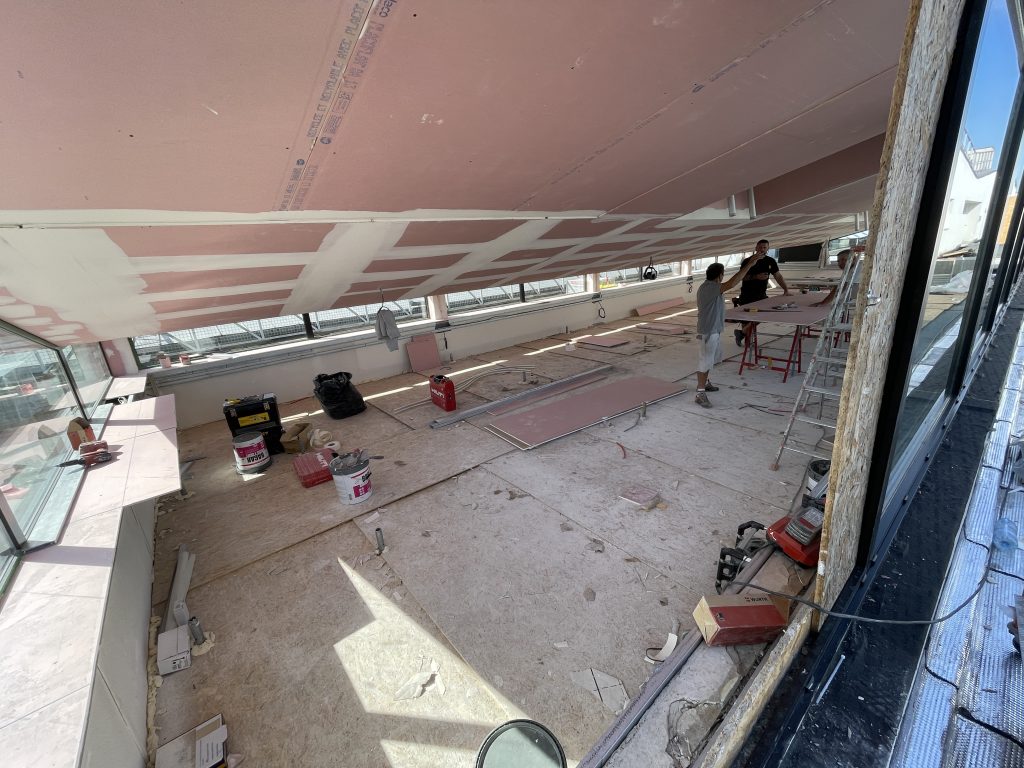 Une verrière de l'UTBM en cours de rénovation, la plateforme en bois qui constitue le sol est soutenue par un échafaudage sur toute la hauteur centrale du bâtiment.